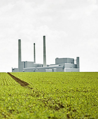 Bild zeigt einen Industriebetrieb; im Vorgergrund ist ein Getreidefeld zu sehen.