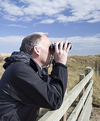 Bild zeigt einen Mann mit Fernglas vor den Augen; er betrachtet die Landschaft.