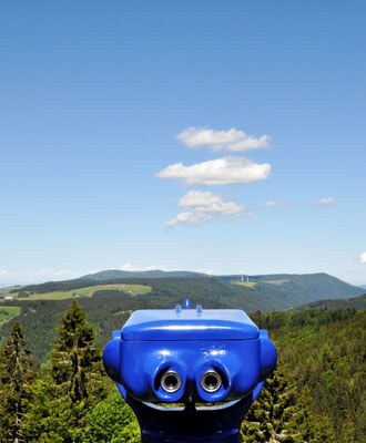 Bild zeigt ein Fernglas, das über eine Hügellandschaft blickt