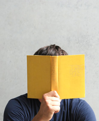 Bild zeigt einen Menschen, der sein Gesicht hinter einem Buch versteckt